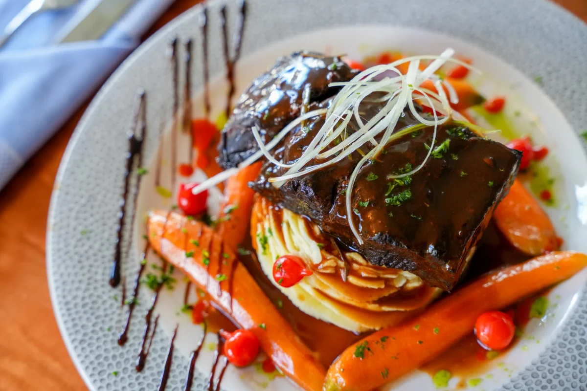 Braised short rib glazed in dark sauce over mashed potatoes with baby carrots, red peppers, crispy leek threads and balsamic drizzle