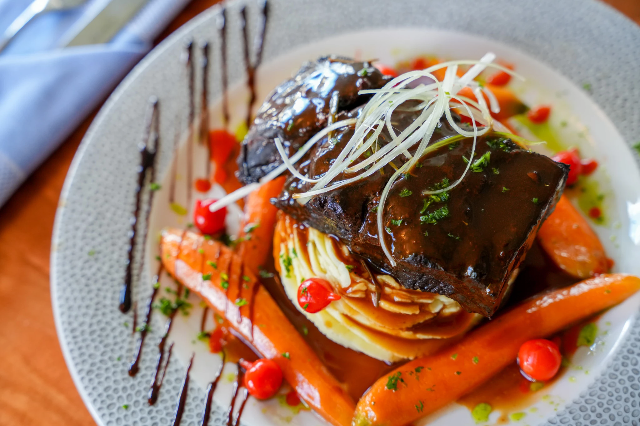 Braised short rib glazed in dark sauce over mashed potatoes with baby carrots, red peppers, crispy leek threads and balsamic drizzle