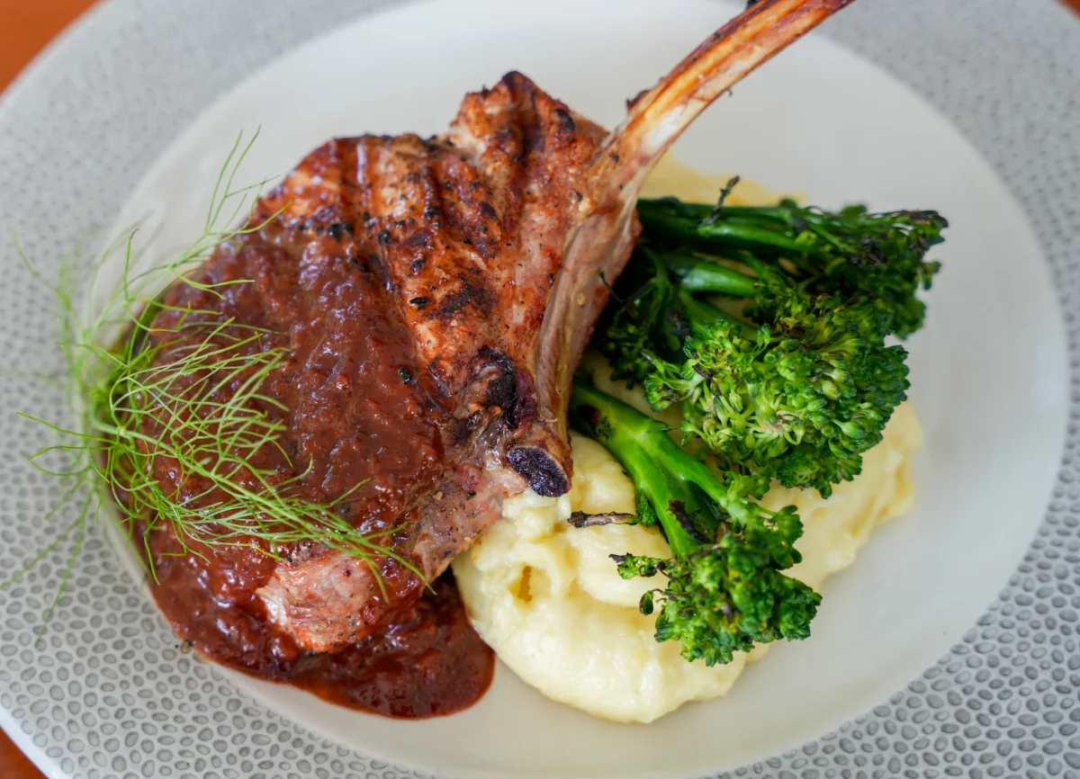 Grilled frenched bone-in chop under a dark cherry sauce, plated with charred broccolini, whipped potatoes and fennel fronds