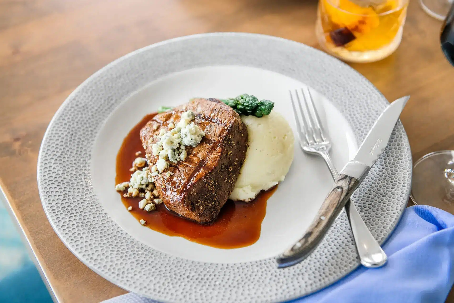 A steak on a plate with sauce, veg, and silverware